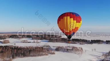 空中拍摄的人们乘坐一个明亮的大气球飞越冬季森林。推拉缩放效果。